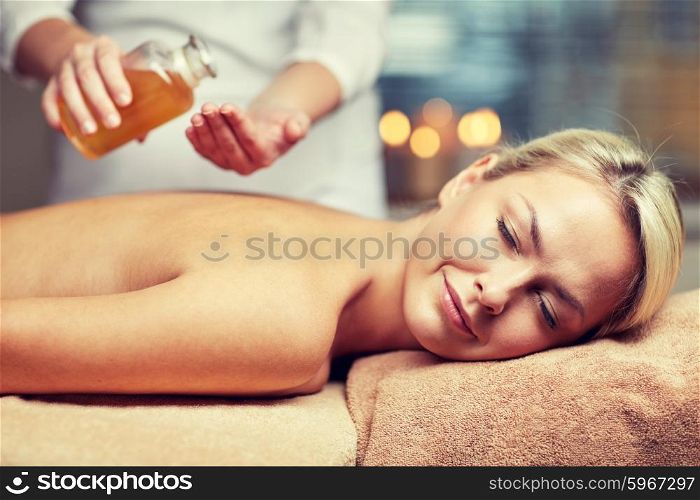 people, beauty, spa, healthy lifestyle and relaxation concept - close up of beautiful young woman lying with closed eyes on massage table and therapist holding oil bottle in spa
