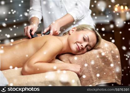 people, beauty, spa, healthy lifestyle and relaxation concept - close up of beautiful young woman having hot stone back massage in spa with snow effect