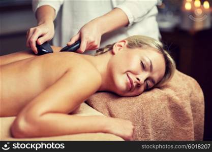 people, beauty, spa, healthy lifestyle and relaxation concept - close up of beautiful young woman having hot stone massage in spa