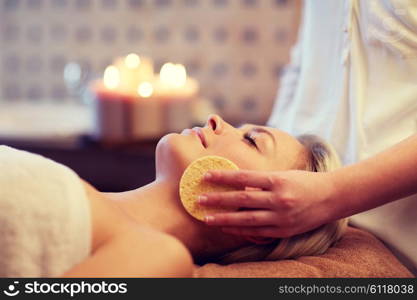 people, beauty, spa, healthy lifestyle and relaxation concept - close up of beautiful young woman lying with closed eyes and having face massage with sponge in spa