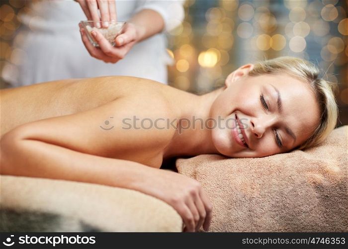 people, beauty, spa, massage and relaxation concept - close up of beautiful young woman lying with closed eyes and therapist holding salt bowl in spa