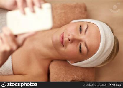 people, beauty, spa, technology and relaxation concept - close up of beautiful smiling young woman lying with smartphone in spa