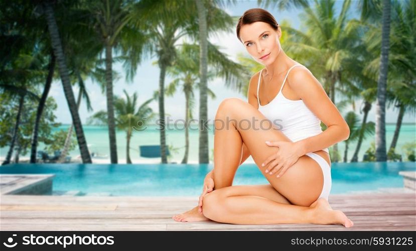 people, beauty, spa, travel and resort concept - beautiful woman in cotton underwear touching her hips over swimming pool on beach with palms background