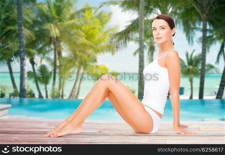 people, beauty, spa, travel and resort concept - beautiful woman in cotton underwear over swimming pool on beach with palms background