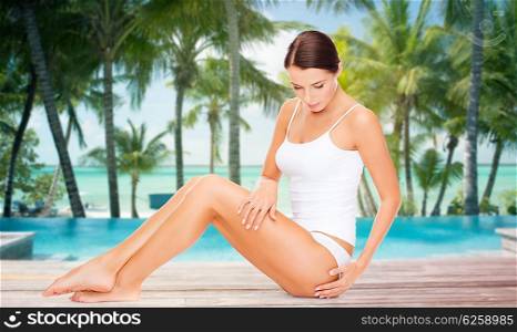 people, beauty, spa, travel and resort concept - beautiful woman in cotton underwear touching her hips over swimming pool on beach with palms background