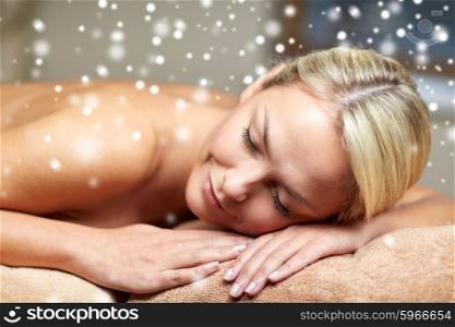 people, beauty, spa, winter and relaxation concept - beautiful young woman lying on massage table in spa salon with snow effect