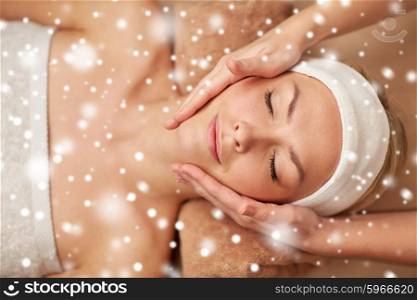 people, beauty, spa, winter and relaxation concept - close up of beautiful young woman lying with closed eyes and having face massage in spa with snow effect