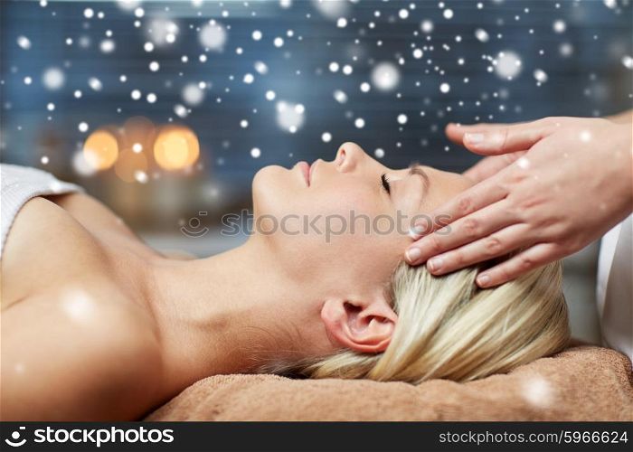 people, beauty, spa, winter and relaxation concept - close up of beautiful young woman lying with closed eyes and having face or head massage in spa with snow effect