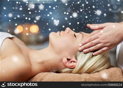people, beauty, spa, winter and relaxation concept - close up of beautiful young woman lying with closed eyes and having face or head massage in spa with snow effect