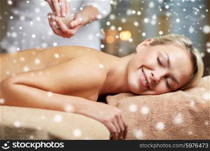 people, beauty, spa, winter and relaxation concept - close up of beautiful young woman lying with closed eyes and therapist holding salt bowl in spa with snow effect