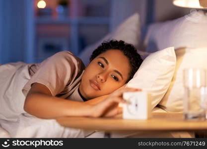 people, bedtime and rest concept - african american woman awaking because of alarm clock at night. woman awaking because of alarm clock at night