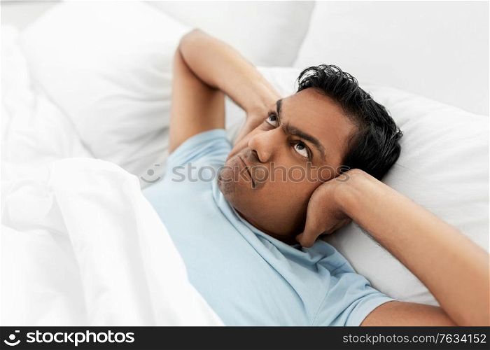 people, bedtime and rest concept - annoyed indian man lying in bed at home and covering ears. annoyed indian man lying in bed and closing ears