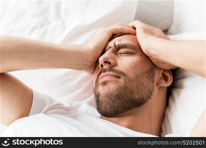 people, bedtime and rest concept - close up of man lying in bed at home suffering from headache or hangover. close up of man in bed suffering from headache