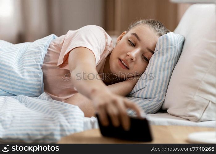 people, bedtime and rest concept - girl picking smartphone from bed table at home. girl picking smartphone from bed table at home