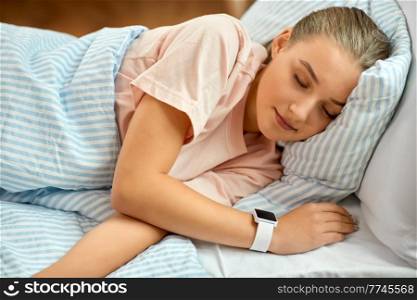people, bedtime and rest concept - girl with smart watch sleeping in bed at home. girl with smart watch sleeping in bed at home