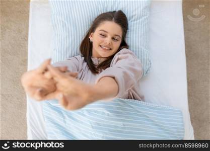 people, bedtime and rest concept - happy smiling teenage girl stretching in bed at home in morning. happy smiling girl stretching in bed