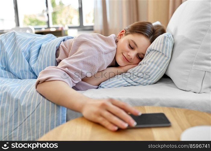 people, bedtime and rest concept - happy smiling teenage girl with smartphone lying in bed at home. happy girl with smartphone in bed at home