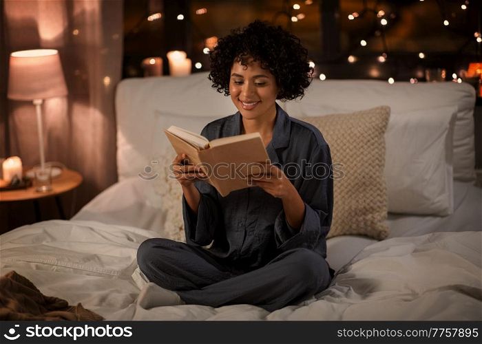 people, bedtime and rest concept - happy smiling woman in pajamas reading book sitting in bed at night. happy woman reading book sitting in bed at night