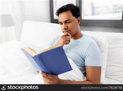 people, bedtime and rest concept - indian man reading book in bed at home. indian man reading book in bed at home