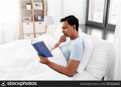 people, bedtime and rest concept - indian man reading book in bed at home. indian man reading book in bed at home