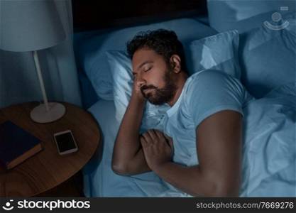 people, bedtime and rest concept - indian man sleeping in bed at home at night. indian man sleeping in bed at home at night