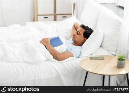 people, bedtime and rest concept - indian man with book sleeping in bed at home. indian man with book sleeping in bed at home