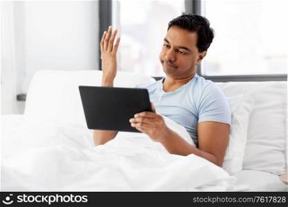 people, bedtime and rest concept - indian man with tablet pc computer lying in bed at home. indian man with tablet pc in bed at home