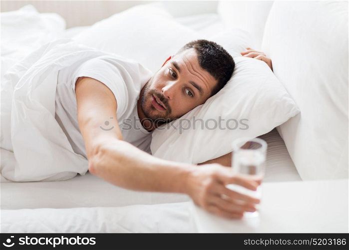 people, bedtime and rest concept - man in bed and reaching to glass of water at home. man in bed and reaching to glass of water at home