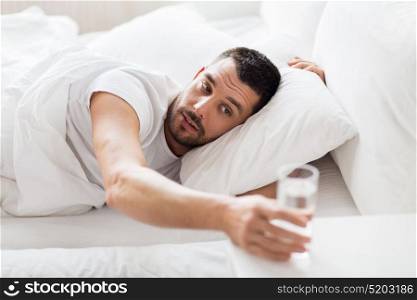 people, bedtime and rest concept - man in bed and reaching to glass of water at home. man in bed and reaching to glass of water at home