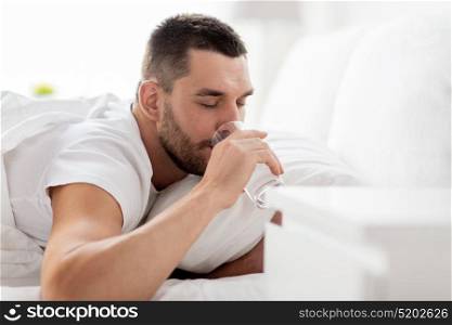 people, bedtime and rest concept - man in bed drinking from glass of water at home. man in bed with glass of water drinking at home
