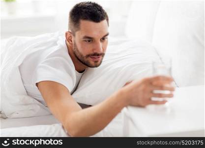 people, bedtime and rest concept - man in bed with glass of water at home. man in bed with glass of water at home