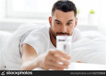 people, bedtime and rest concept - man in bed with glass of water at home. man in bed with glass of water at home