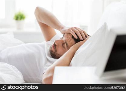 people, bedtime and rest concept - man lying in bed at home suffering from headache or hangover. man in bed at home suffering from headache