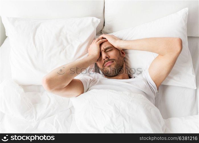 people, bedtime and rest concept - man lying in bed at home suffering from headache or hangover. man in bed at home suffering from headache