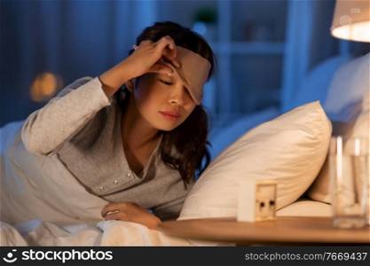 people, bedtime and rest concept - sleepy asian woman with clock lying in bed at night. asian woman with clock lying in bed at night