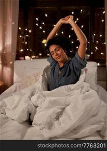 people, bedtime and rest concept - sleepy woman in pajamas stretching in bed at night. sleepy woman stretching in bed at night