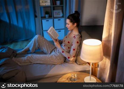 people, bedtime and rest concept - teenage girl reading book in bed at home at night. teenage girl reading book in bed at home