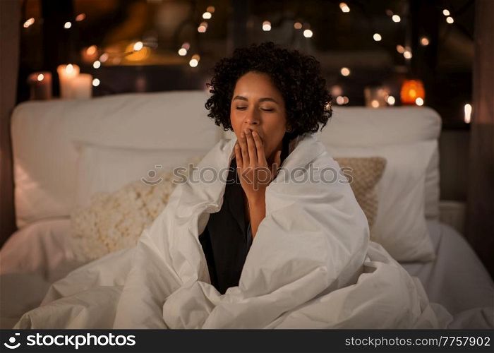 people, bedtime and rest concept - tired sleepy woman wrapped in blanket yawning sitting in bed at night. yawning woman wrapped in blanket in bed at night