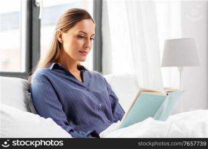 people, bedtime and rest concept - young woman reading book in bed at home. young woman reading book in bed at home