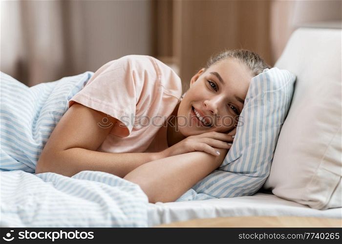 people, bedtime and sleeping concept - happy smiling awake girl lying in bed at home. happy smiling awake girl lying in bed at home
