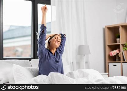 people, bedtime and sleeping concept - happy woman stretching in bed at home. happy woman stretching in bed at home