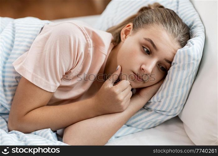 people, bedtime and sleeping concept - sad girl lying in bed at home. sad girl lying in bed at home