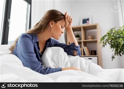 people, bedtime and sleeping concept - sleepy or stressed woman sitting in bed at home. sleepy or stressed woman sitting in bed at home