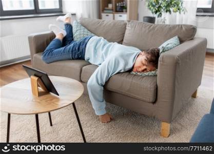 people, boredom and depression concept - bored or lazy young man with tablet pc computer lying on sofa at home. bored man with tablet pc lying on sofa at home