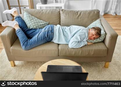 people, boredom and depression concept - bored or lazy young man with laptop computer lying on sofa at home. bored man with laptop lying on sofa at home