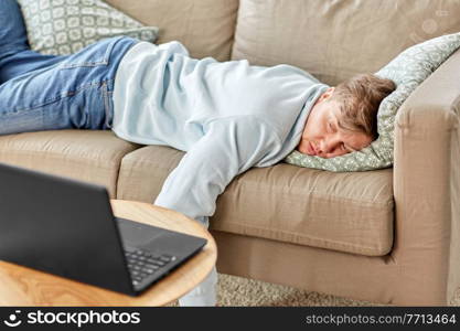 people, boredom and depression concept - bored or lazy young man with laptop computer lying on sofa at home. bored man with laptop lying on sofa at home