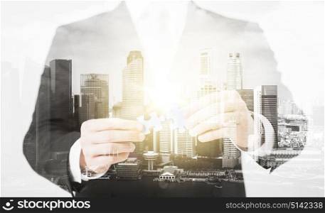 people, business and management concept - close up of businessman with puzzle pieces over city with double exposure. close up of businessman with puzzle pieces