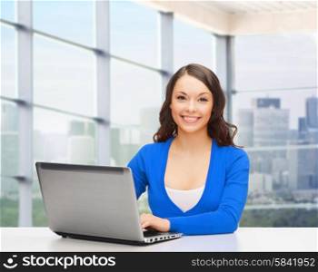 people, business and technology concept - smiling woman in blue clothes with laptop computer sitting at table over office window background
