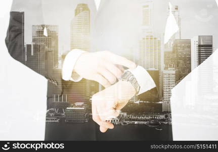 people, business and time concept - close up of businessman with wristwatch over city with double exposure. close up of businessman with wristwatch