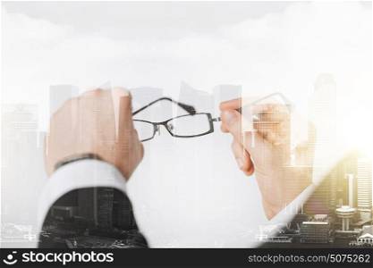 people, business and vision concept - close up of businessman hands holding glasses over city with double exposure. close up of businessman hands holding glasses